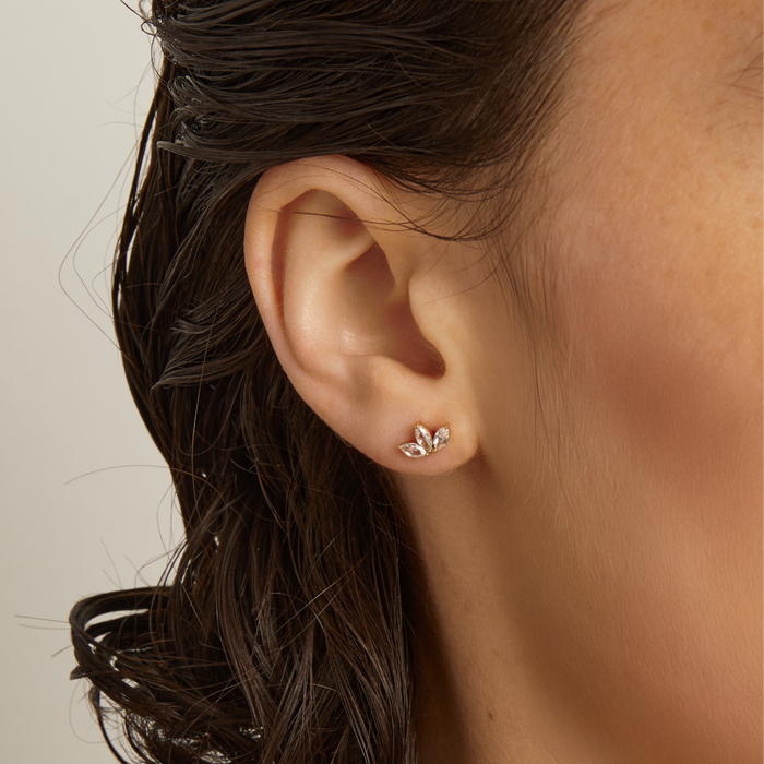Model. Close-up of an ear wearing a diamond earring with dark hair and neutral background