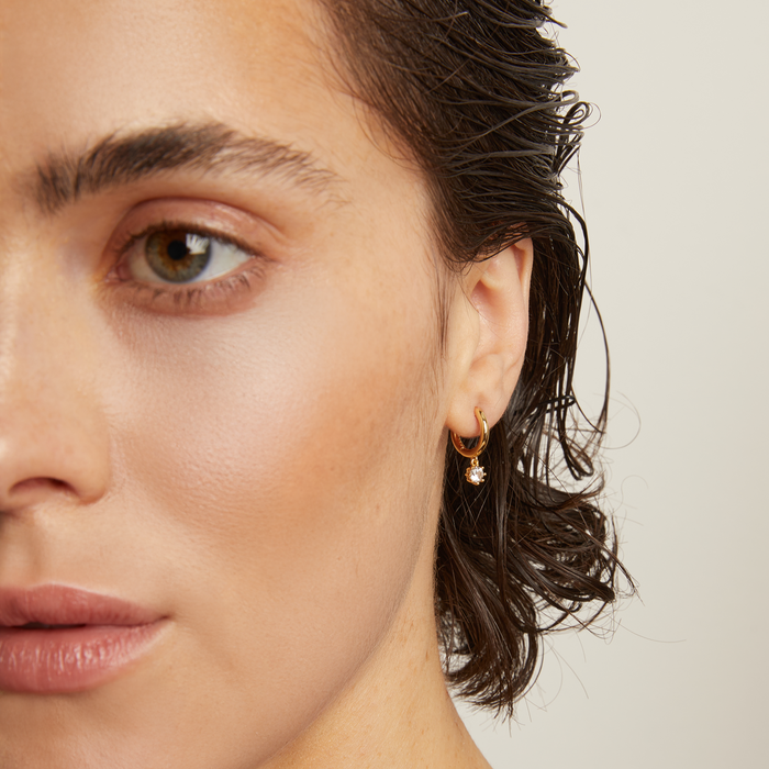 Model. Close-up of a person wearing a gold earring and necklace against a neutral background