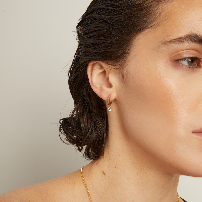 Model. Close-up of a woman wearing a gold necklace against a neutral background