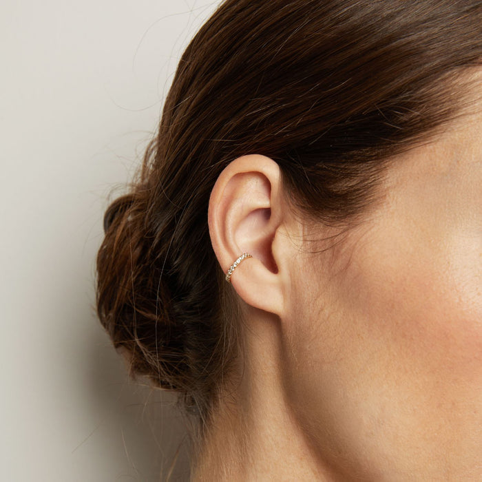 Model. Close-up of an ear wearing a delicate earring with a plain background
