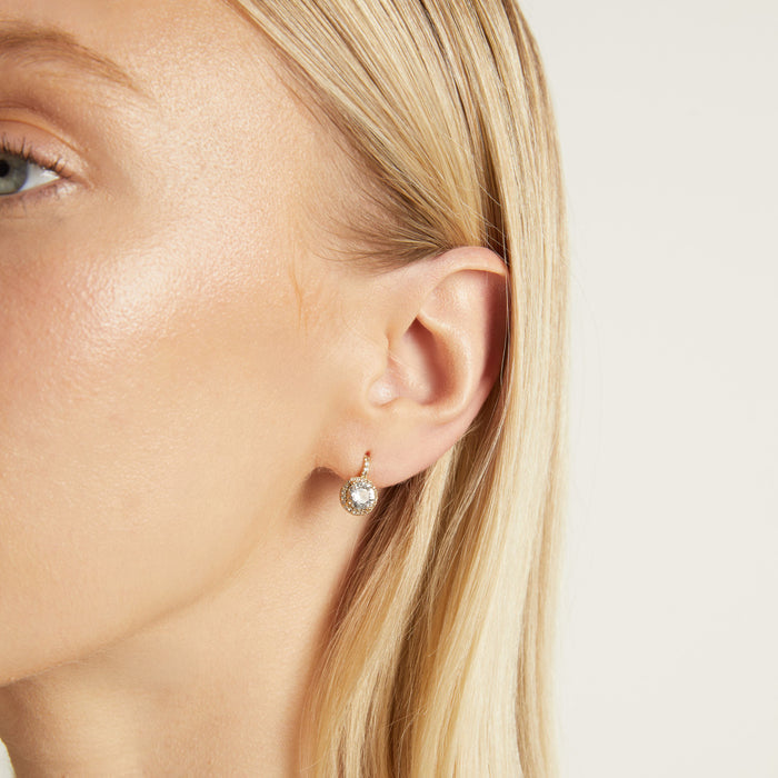 Model. Close-up of a person wearing a diamond earring on a plain background