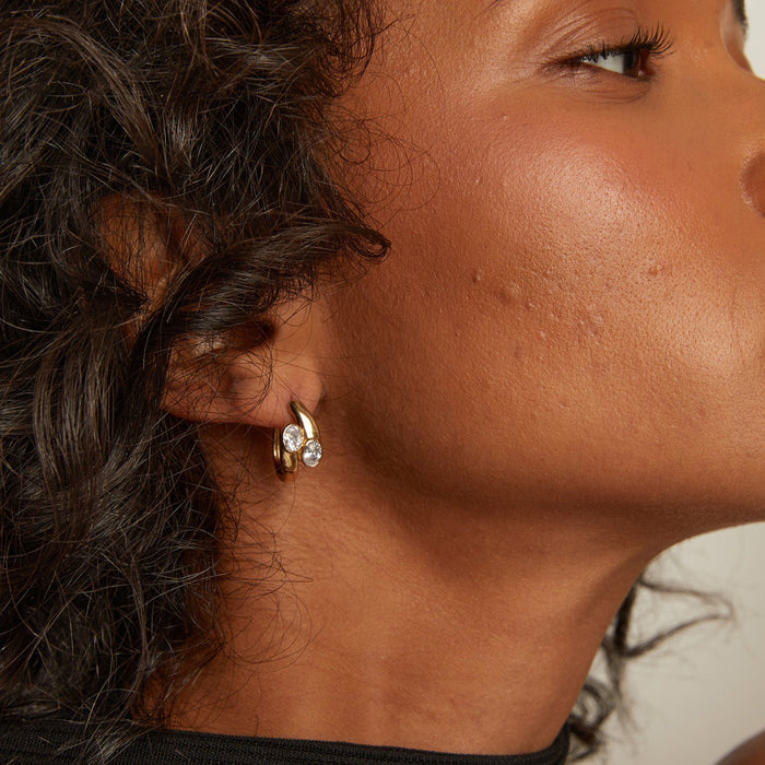 Model. Close-up of a woman wearing gold hoop earrings with a neutral background