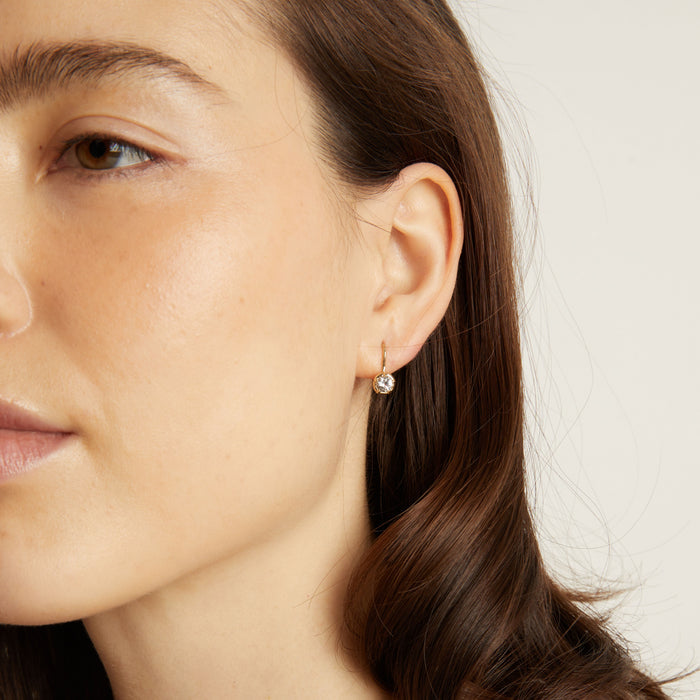 Model Close-up of a woman wearing a gold earring with a clear gemstone on a neutral background