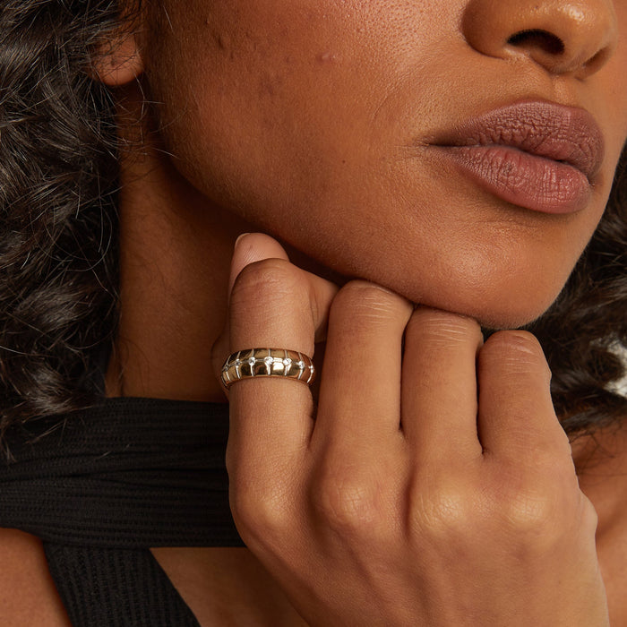 Model. Close-up of a person's hand with a gold ring on their finger, touching their chin.