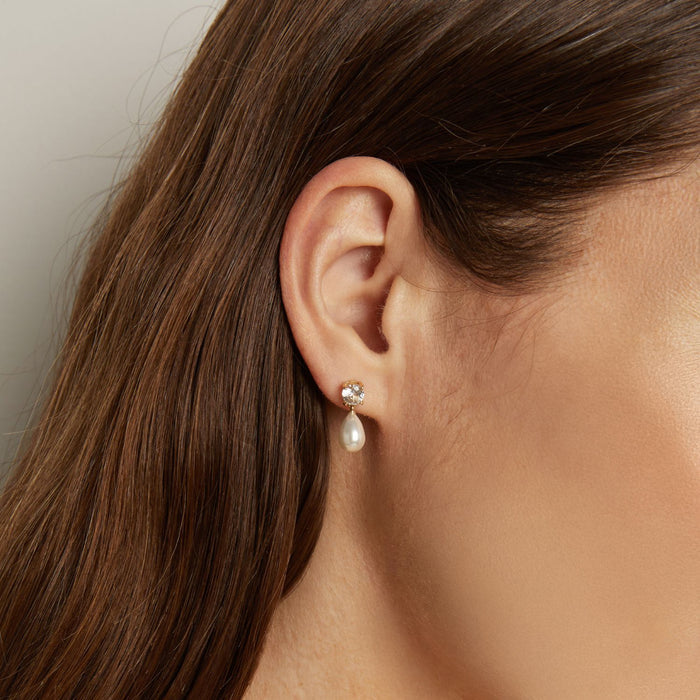 Model. Close-up of an ear wearing a pearl earring with a neutral background