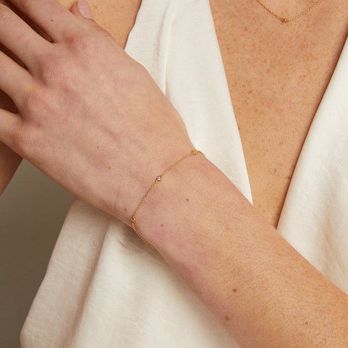 Model. Person wearing a delicate gold bracelet and necklace against a neutral background