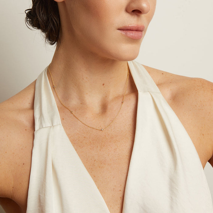 Model. Close-up of a woman wearing a gold necklace with a plain background