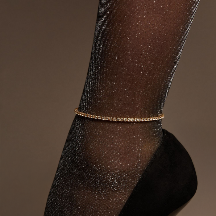 Model. Black high heeled shoes worn with sheer black stockings and a tennis anklet on a neutral background.