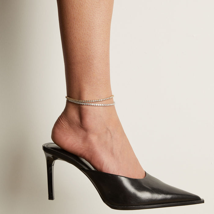 Model. Tennis anklets and black high heeled shoe worn on a foot with a neutral background.