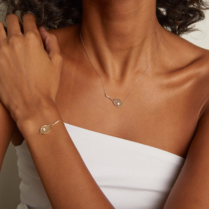 Close-up of a person wearing a gold necklace and bracelet on a neutral background