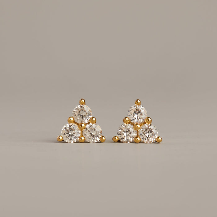 Model. Pair of gold and diamond triangle-shaped earrings on a gray background