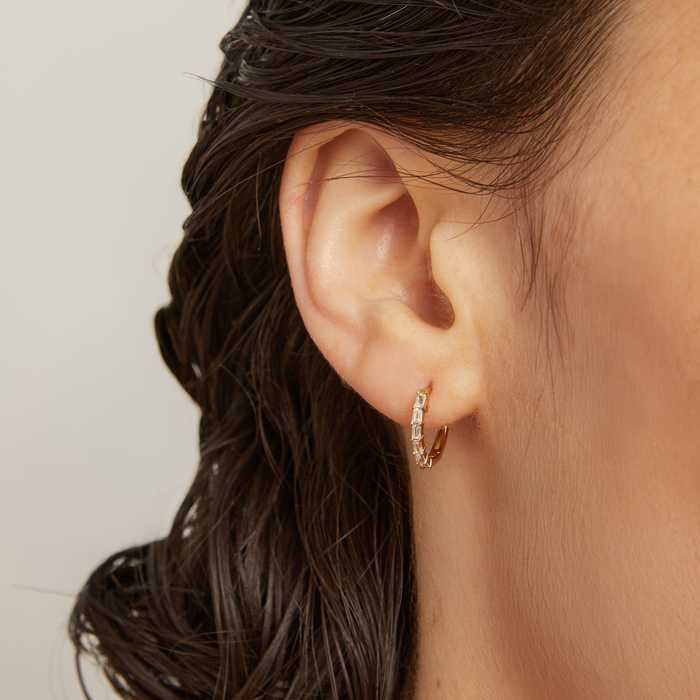 Model. Close-up of an ear wearing a gold hoop earring with hair styled in braids.