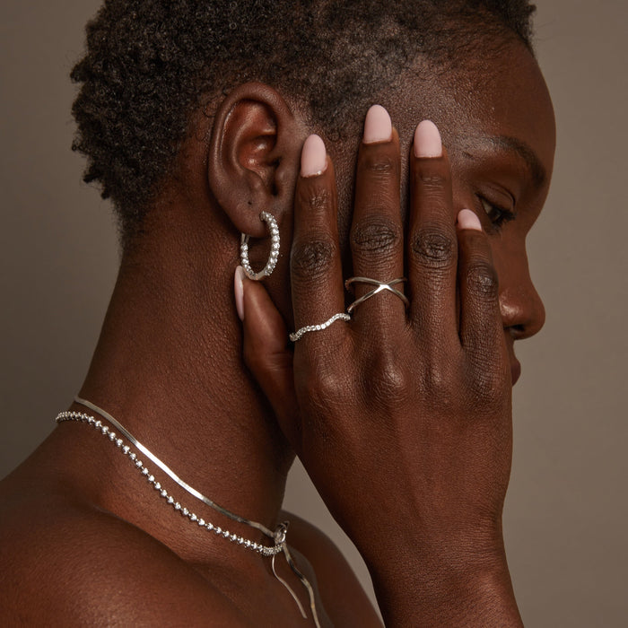 Model. Woman wearing silver jewelry including earrings, rings, and necklaces on a brown background