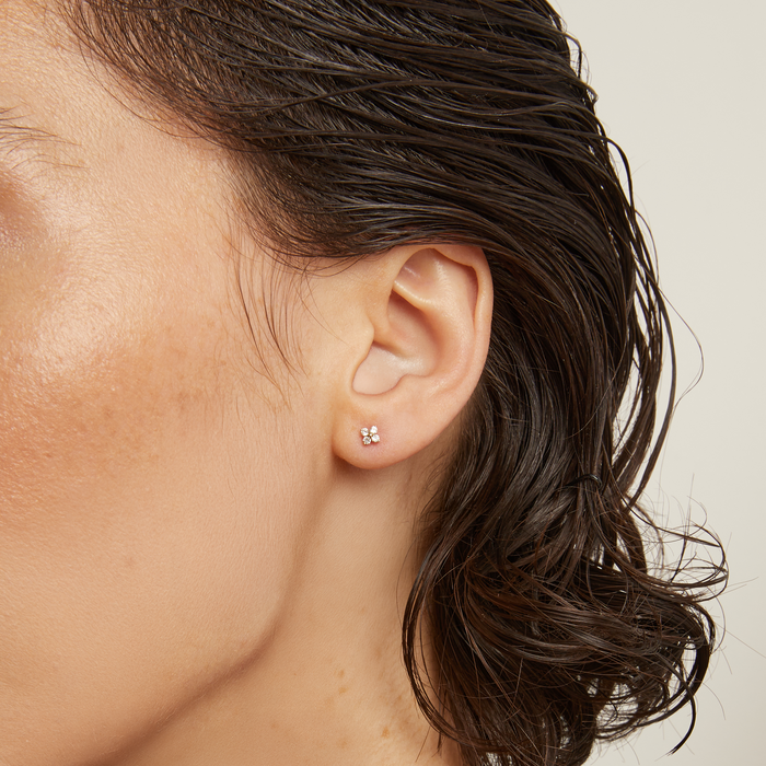 Model. Close-up of a person wearing a gold necklace and earring against a neutral background
