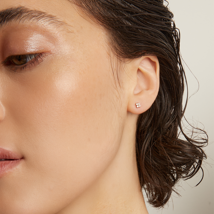 Model. Close-up of a person wearing a gold necklace and earring against a neutral background