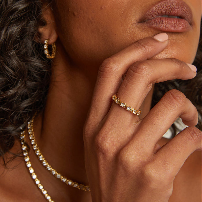 Model. Close-up of a woman wearing a gold ring and necklace, with her hand near her face.