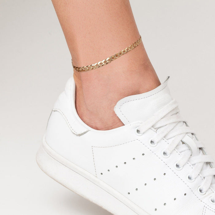 Model. Close of up of foot with white sneaker and gold chain anklet