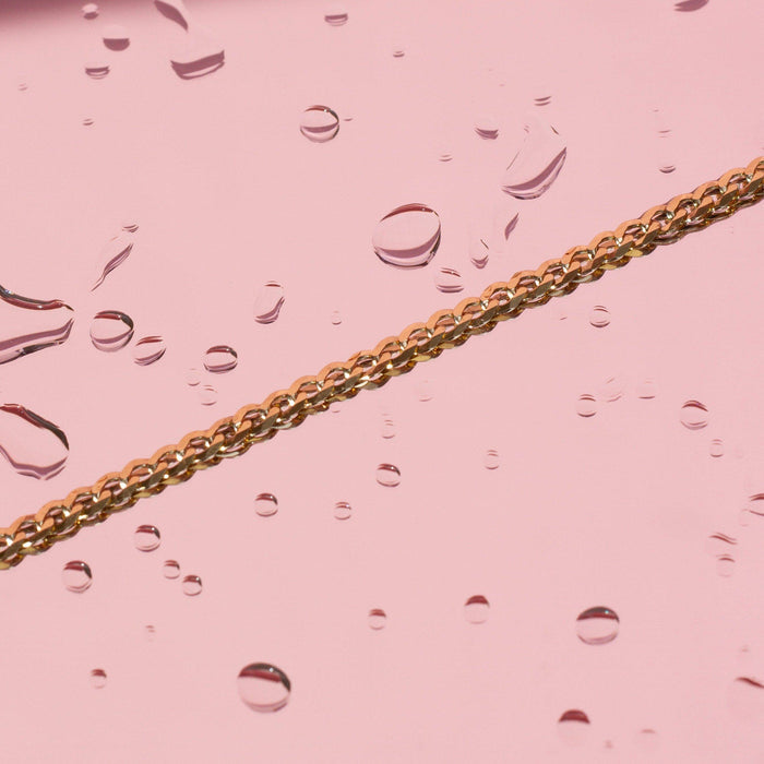 Flatlay Model. Gold chain bracelet on pink background with water drops around it