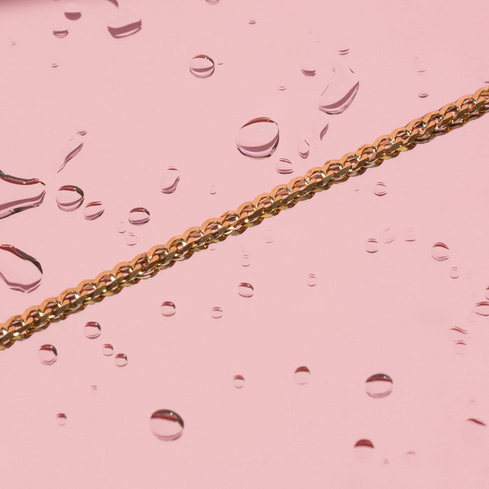 Flatlay Model. Gold chain necklaces on pink background with water drops on it