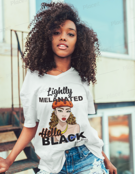 A woman with voluminous curly hair wearing a white graphic t-shirt that reads 'Lightly Meltinged' and 'Hello BLACK' with an illustration of a woman in a beret, paired with distressed denim shorts.