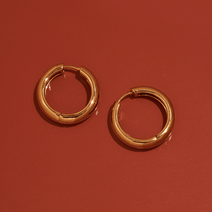 Flatlay Model. Gold hoop earrings on orange background
