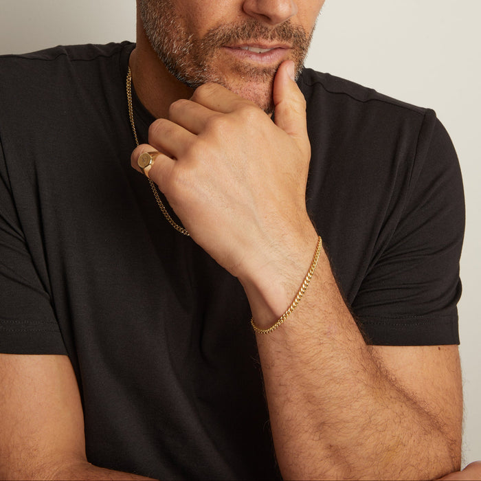 Man wearing a black shirt with gold jewelry on a neutral background