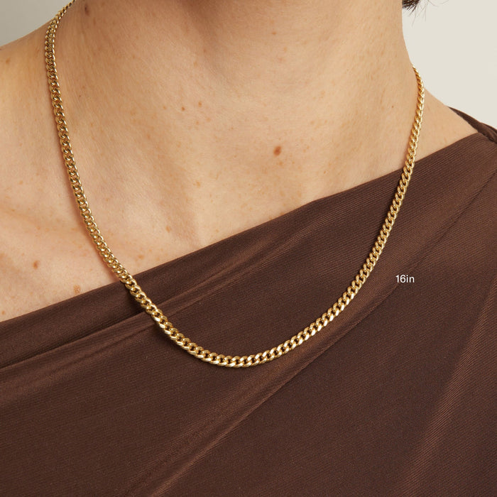 Model. Gold chain necklace worn by a person with a brown top on a neutral background