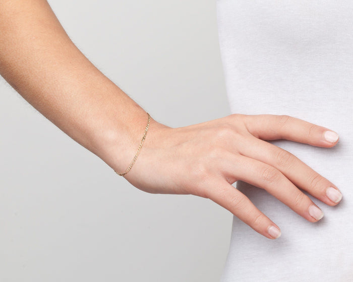 Model. Close up of woman wearing gold chain bracelet on white background