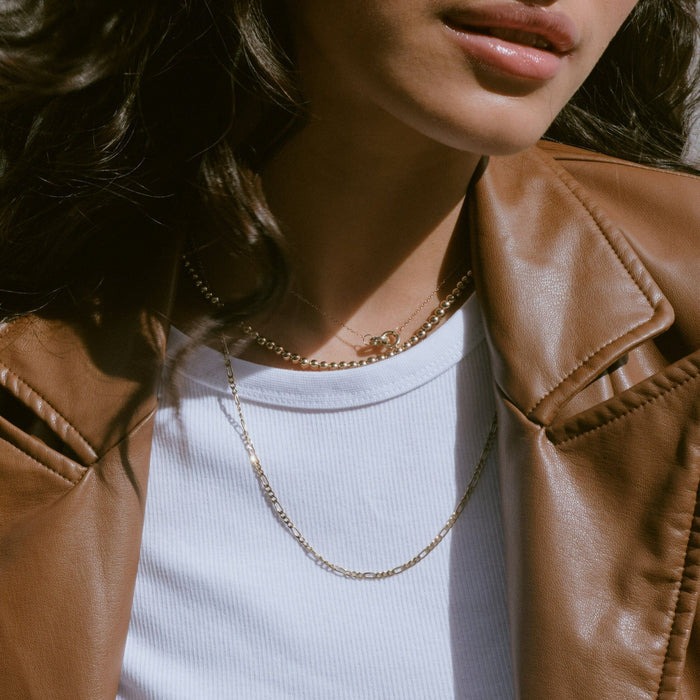 Lifestyle Model. Close up of a woman wearing stacked gold necklaces with leather jacket and white shirt