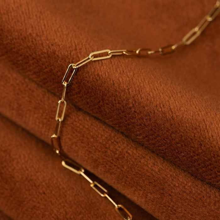 Model. Close up of gold chain necklace on orange suede background