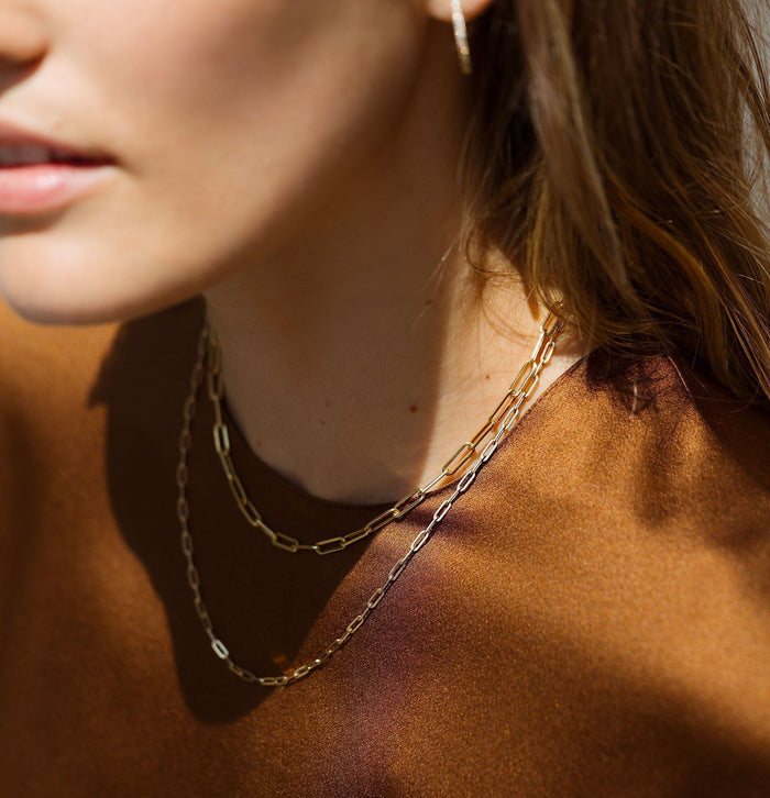 Lifestyle Model. Close up of woman wearing two chain necklaces with orange top