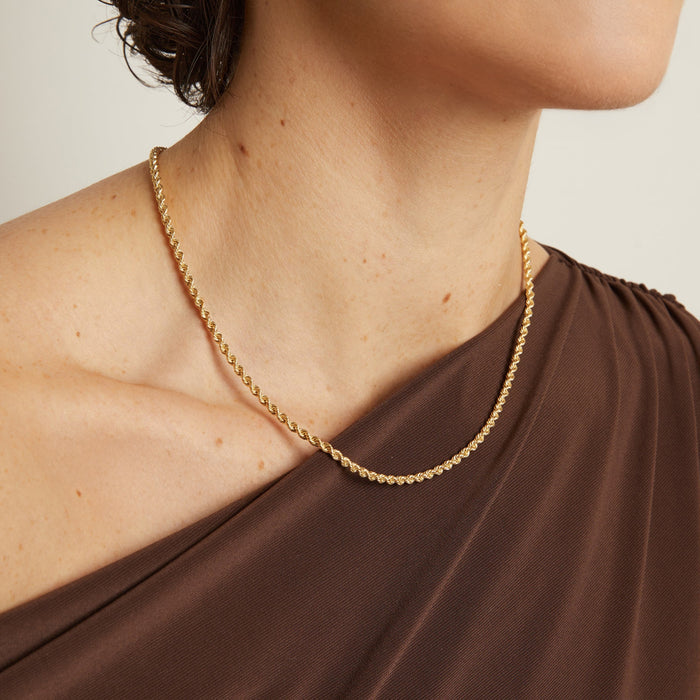 Model. Gold chain necklace worn by a person with a neutral background