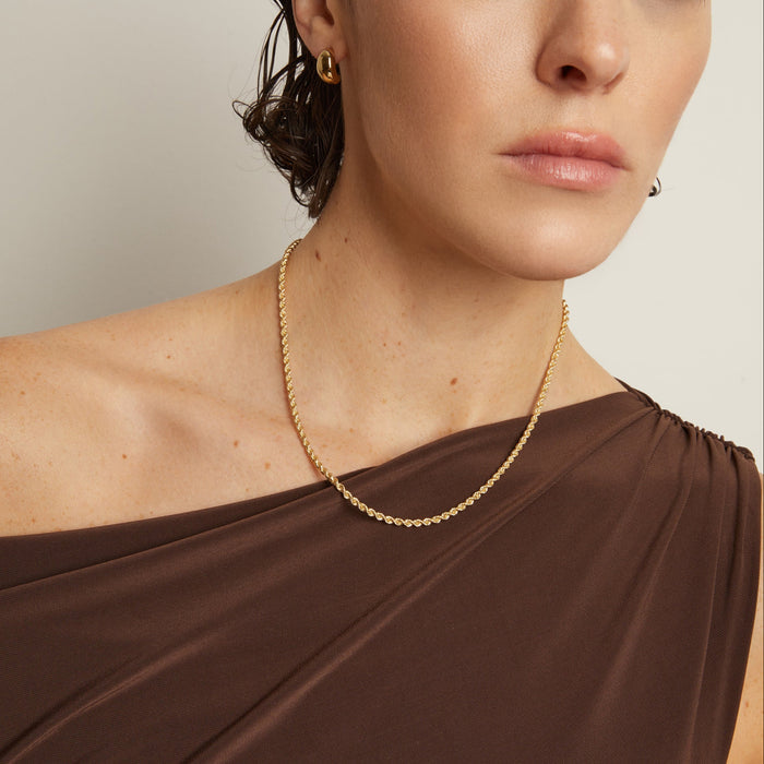 Model. Woman wearing a gold necklace and earrings against a neutral background