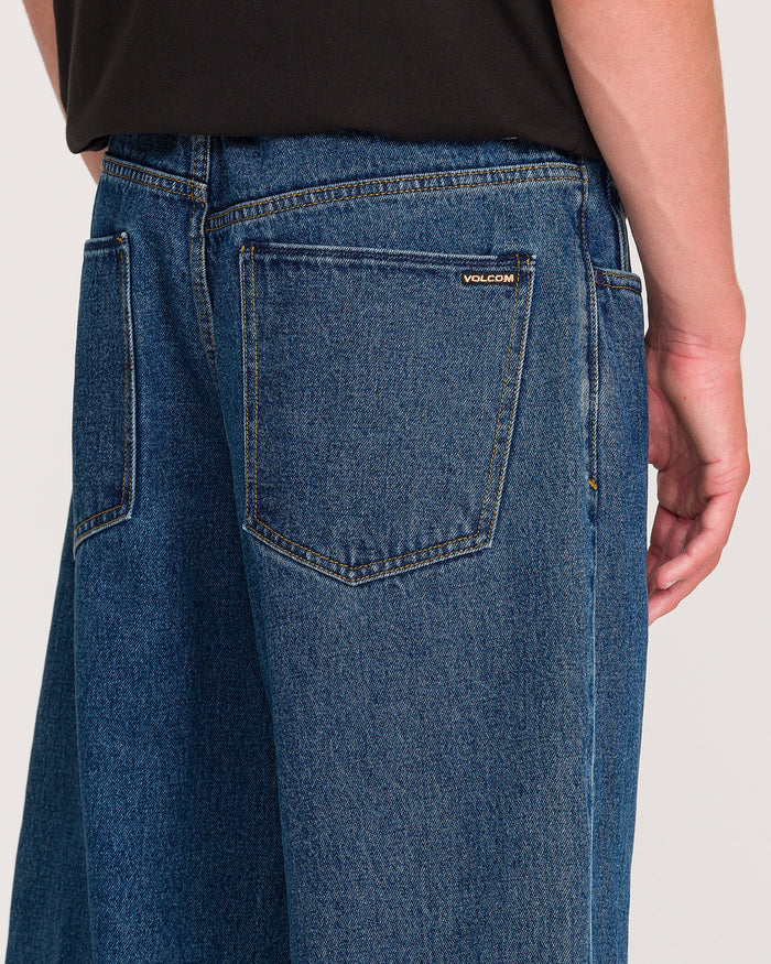 A person is shown from the waist down wearing Volcom Men’s Billow Denim Pants in a loose fit, with attention on the back pocket that features a small Volcom brand label alongside a black shirt.