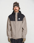A man with a mustache wears the Volcom Men’s Buckthreeeighty Jacket, which features PFAS-free DWR, along with a patterned beanie and gloves. He stands against a plain white background, looking slightly to the side.