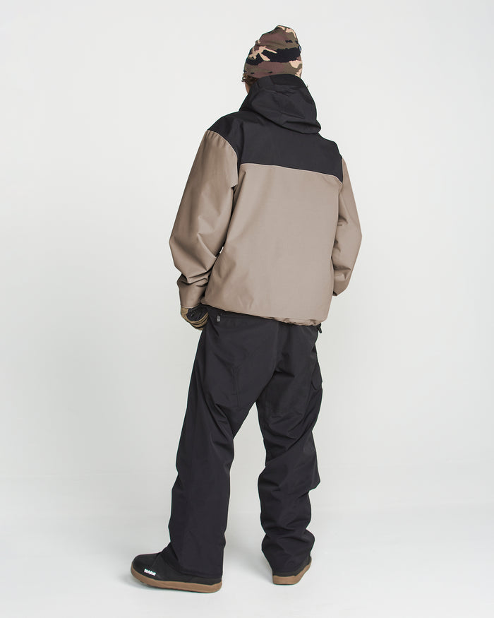A person stands facing away, wearing the Volcom Men’s Buckthreeeighty Jacket with PFAS-free DWR, black pants, black shoes, gloves, and a brown camo beanie against a plain white background.