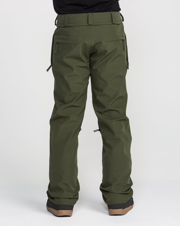 A person wearing olive green Volcom Men’s Freakin Snow Chino Pants, renowned for their waterproof breathable fabric, and brown-soled shoes stands facing away to showcase the back view of these men’s snow pants against a plain white background.