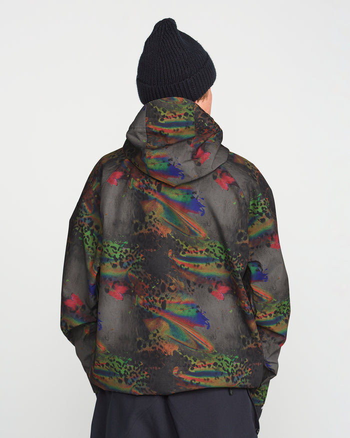 A person wearing a black knit beanie and the Volcom Men’s Hossegor 20K Pullover—a hooded jacket featuring a colorful, abstract pattern crafted from recycled V-Science shell—stands facing away against a plain white background.