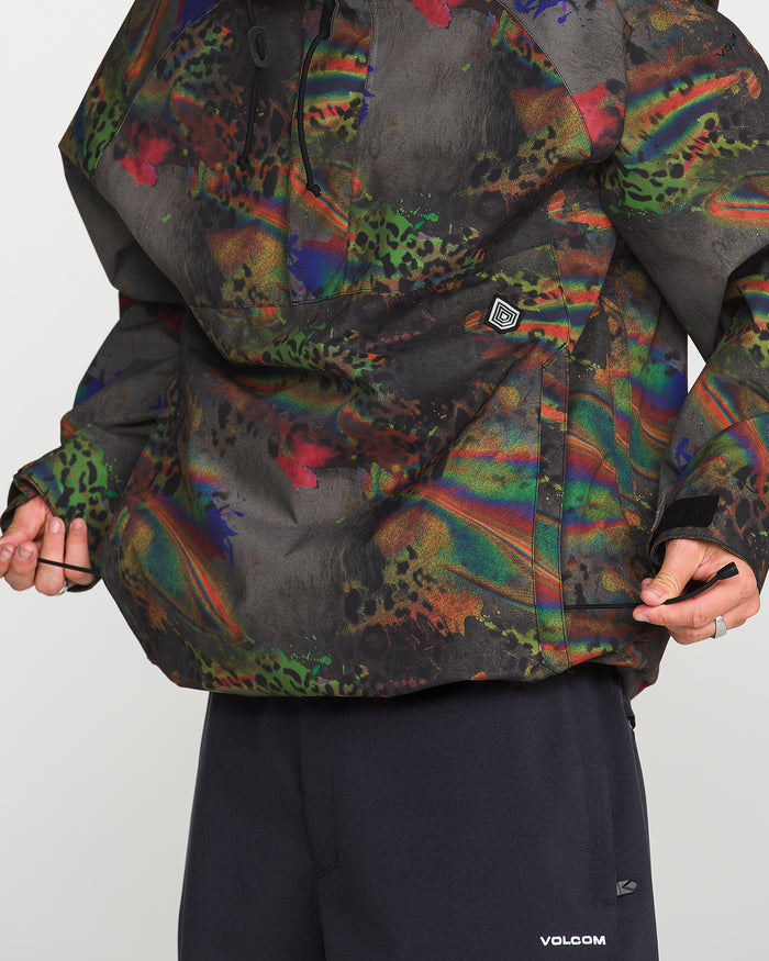 A person wears the Volcom Men’s Hossegor 20K Pullover—an oversized jacket showcasing a vibrant, abstract design and constructed from recycled V-Science shell with PFAS-free DWR. Black pants adorned with a small Volcom logo complete the look. Only the torso and part of the arms are visible; the individual’s face remains out of frame.