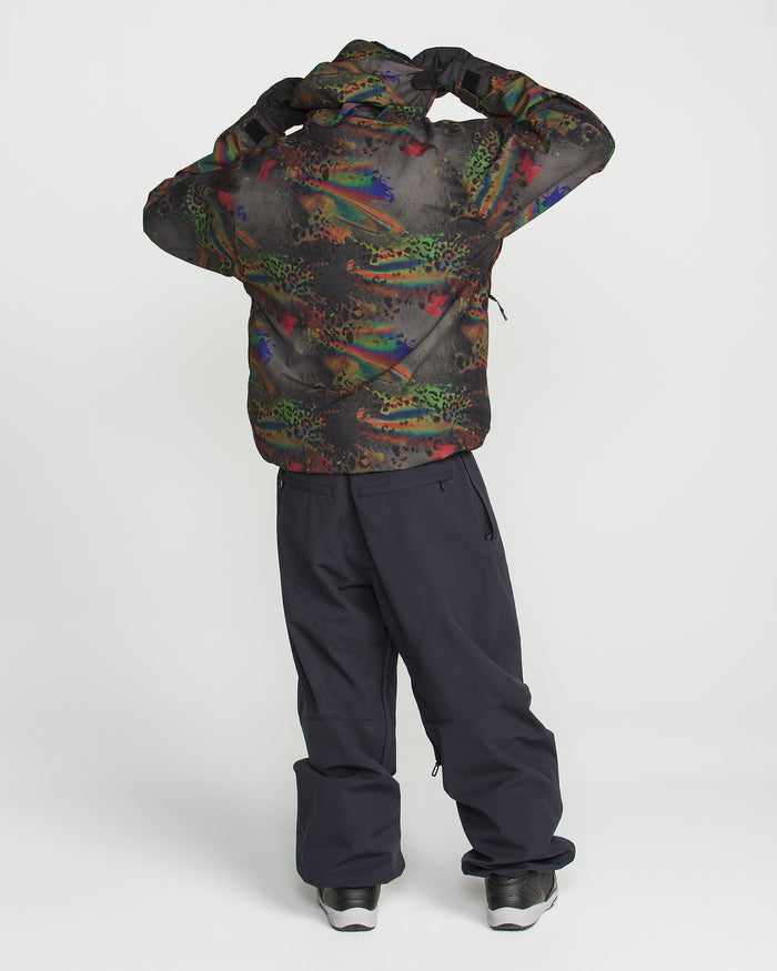 A person wearing the Volcom Men’s Hossegor 20K Pullover, featuring a colorful, patterned design crafted from recycled V-Science shell, and black pants stands facing away, adjusting their hood with both hands against a plain white background.