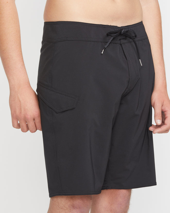 A man models Volcom's Men's Lido Solid Mod 20 black board shorts, featuring a drawstring waist and side flap pocket, standing against a plain white background. Only his torso and upper legs are shown.