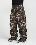 A person wearing Volcom Men’s Nwrk 20K Baggy Pants in a camouflage cargo style and black snow boots, standing against a white background; only the lower half of their body is visible.