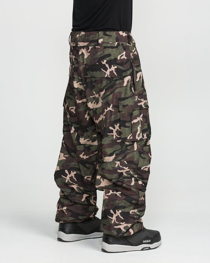 A person wearing Volcom Men’s Nwrk 20K Baggy Pants styled like snowboard pants, paired with black sneakers, stands against a plain white background with only the lower half of the body visible.