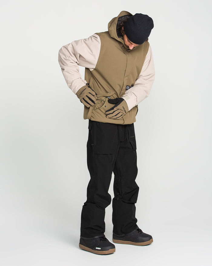 Wearing the Volcom Men’s Roan Bib, this person stands against a plain white background, dressed in black pants with adjustable suspenders, a beige and tan jacket, gloves, boots, and a dark beanie.