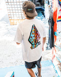 Wearing the Volcom Men's Star Shields Featured Artist Exp Short Sleeve Tee and a cap, a person walks down colorful steps into the sunlit outdoors. The tee’s bold star shields and graphic art add artistic flair to the scene.