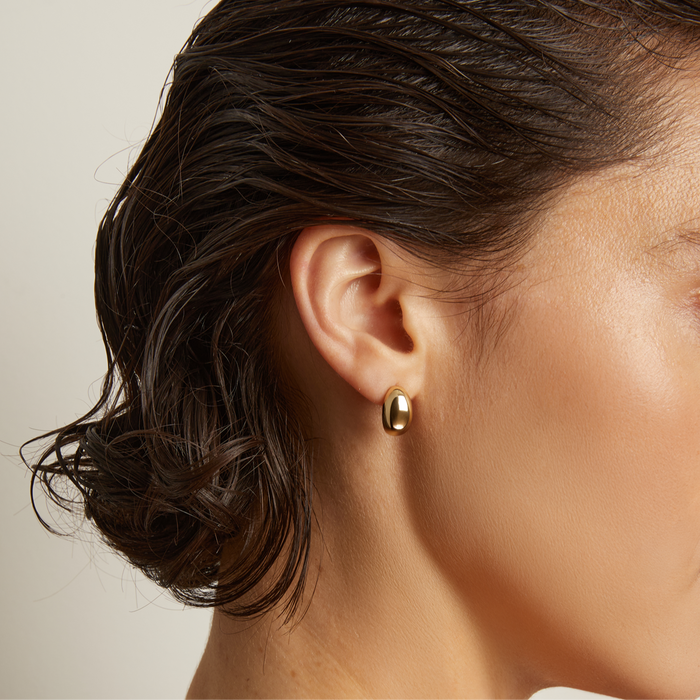 Model. Woman wearing a gold earring and necklace against a neutral background