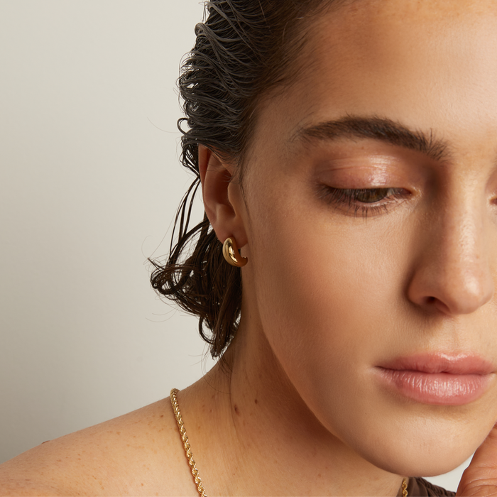 Model. Close-up of a woman with wet hair wearing a gold earring and necklace against a neutral background