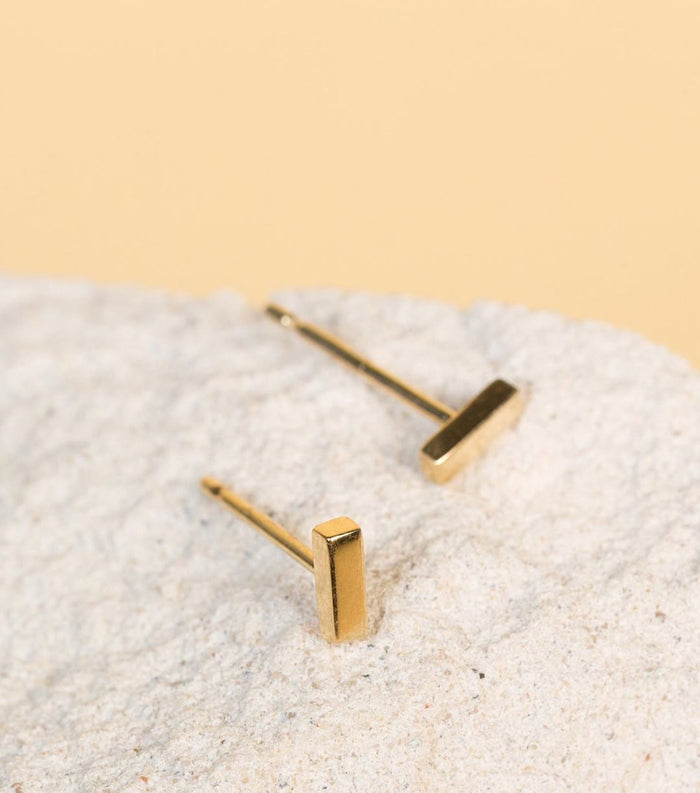 Model. A close-up flatlay shot of two gold bar stud earrings