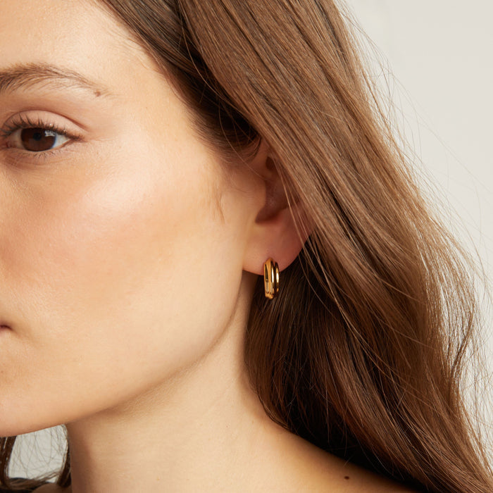 Model. Close up of a person wearing gold hoop earrings.