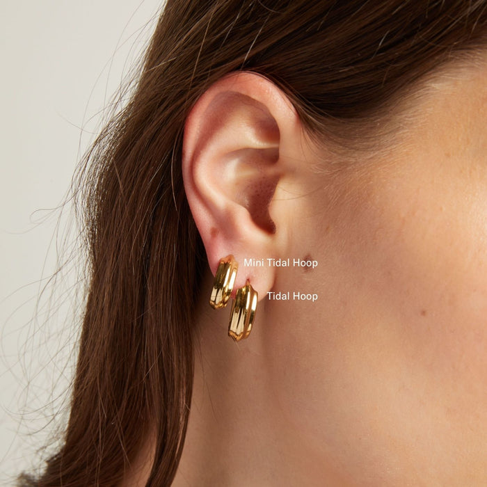 Model. Close up of a woman wearing gold hoop earrings against a neutral background